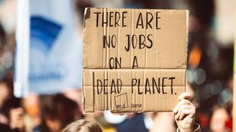 Une personne tenant une pancarte en carton dans une manifestation sur laquelle il est inscrit "there are no jobs on a dead planet"