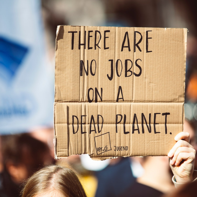 Une personne tenant une pancarte en carton dans une manifestation sur laquelle il est inscrit "there are no jobs on a dead planet"